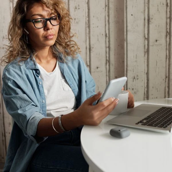 Mujer consultando su celular junto a un computador
